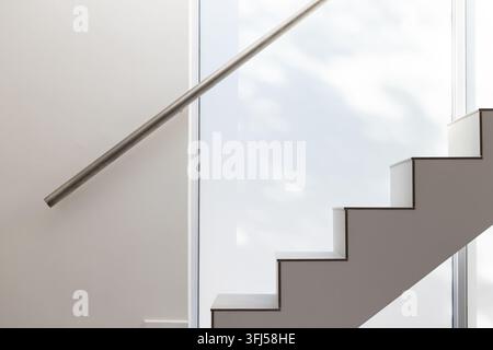 Geometrische gerade Treppe, die nach rechts in einem modernen Treppenhaus mit Edelstahlgeländer und mattiertem Glas aufsteigt Stockfoto
