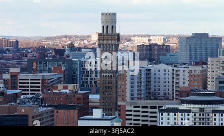 Luftbild-Drohnenaufnahme der Innenstadt von Baltimore, mit historischem Uhrturm, der über modernen Wohn- und Bürogebäuden unter klarem Wintersonnenlicht aufragt Stockfoto