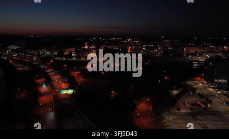 Krümmende Autobahn mit Lichtspuren von Autos führt auf die beleuchtete Kuppel des New Jersey State House im Stadtzentrum von Trenton zu, verstreute Stadtlichter breiten sich über da aus Stockfoto