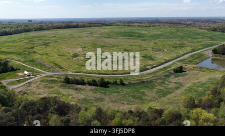 Weite ländliche Farmland-Landschaft mit kurvenreichem Feldweg, grünen Feldern und einem kleinen Teich, umgeben von Bäumen, die idyllische Landschaften in Uni zeigen Stockfoto