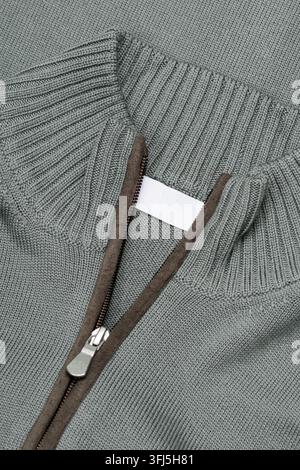 Detaillierte Nahaufnahme eines grauen gestrickten Kleidungsstücks mit gerippter Textur, einem braunen Reißverschlussbesatz und einem Metallreißverschlusskopf. Stockfoto