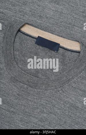 Detaillierte Nahaufnahme eines grauen Strickpullovers mit geripptem Rundhalsausschnitt, kontrastierender Innenverlaufnung und leerem Stoffetikett. Stockfoto
