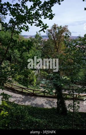 Enge Kopfsteinpflasterwege winden sich durch dichtes Grün mit einem teilweisen Blick auf Prag vom Kinsky-Garten aus. Stockfoto