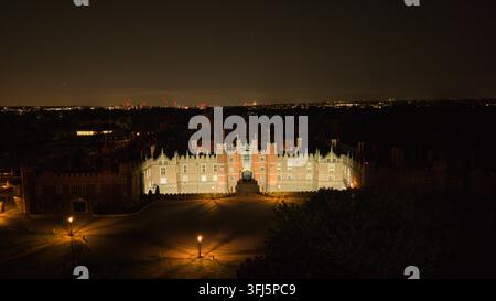 Kingston upon Thames, UK. Ein atemberaubendes nächtliches Luftbild zeigt das prächtige historische Hampton Court Palace, das von warmem Licht brillant beleuchtet wird Stockfoto