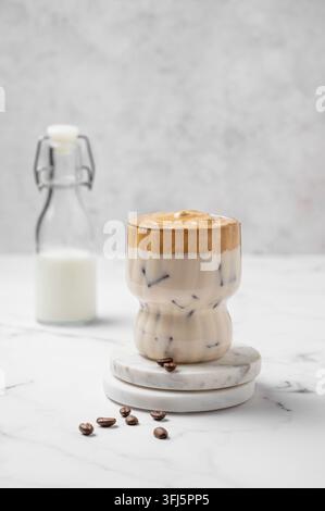 Dalgona-Kaffee. Geschlagener Instant-Eiskaffee in einem Glas mit Kaffeebohnen und Flasche auf Marmorhintergrund. Trendiges süßes Dessertkonzept für Werbung Stockfoto