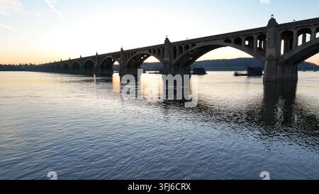 Luftflug über den Susquehanna River während eines goldenen Sonnenuntergangs mit der Silhouette einer Brücke mit Bögen am Abend, Scott Township, Pennsylvania. Stockfoto