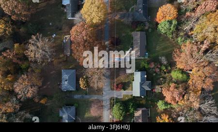 Sanfter Luftfahrt-Drohnenflug über einen von Bäumen gesäumten amerikanischen Vorort, der Häuser und gewundene Straßen inmitten herbstlichen Laubs erfasst, was ein friedliches Leben und Suburbane suggeriert Stockfoto