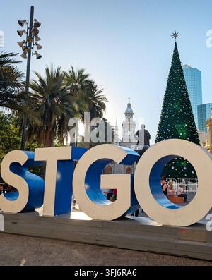 SANTIAGO, CHILE - 03. DEZEMBER 2025: Ein großes STGO-Schild steht in der Nähe eines hohen Weihnachtsbaums auf der Plaza de Armas mit historischen Gebäuden in der Nähe in Santiago, Chil Stockfoto