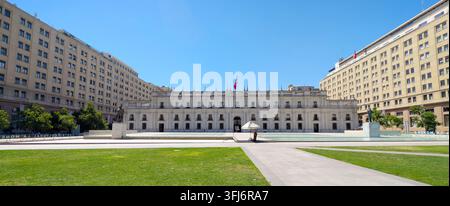 SANTIAGO, CHILE - 03. DEZEMBER 2025: Die große Fassade des La-Moneda-Palastes erhebt sich hinter einem grasbewachsenen Platz an der Plaza de la Ciudadania unter einem klaren blauen Himmel in Stockfoto