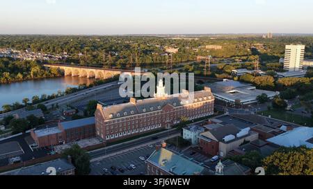 Historisches Gebäude der Rutgers University erhebt sich über dem Campus am Flussufer in New Brunswick, New Jersey, bei Sonnenuntergang, gewölbte Eisenbahnbrücke spannt sich über das Wasser daneben Stockfoto
