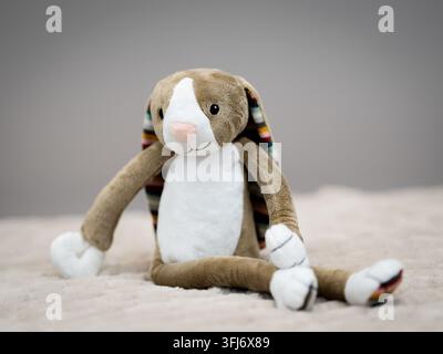 Weiches Plüschkaninchen-Spielzeug sitzt auf einer hellen Decke vor einem neutralen Hintergrund mit geringer Schärfentiefe. Stockfoto