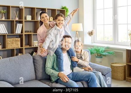 Lächelnde Mutter und Vater mit Töchtern, die auf dem Sofa in einem hellen Wohninterieur spielen Stockfoto