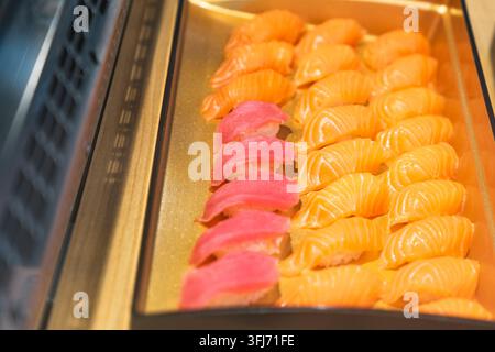 Japanisches Sushi-Esskonzept, Reihen von frischem Lachs- und Thunfisch-Nigiri, angeordnet auf einem goldenen Serviertablett in der Restauranttheke, repräsentierend authentisch Stockfoto