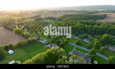 Hohe Luftaufnahme einer weitläufigen ländlichen Nachbarschaft. Ländliche Stadt in Pennsylvania während des Frühlingssonnenuntergangs. Drehende Drohnenansicht zur golden hour, Lititz. Stockfoto