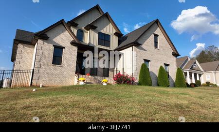 Modernes amerikanisches Vorstadthaus mit Ziegelfassade, gepflegtem Garten und hellen Blumen. Sonniger Sommertag in den USA. Komfort, Stil und zeitgenössischer Nachbar Stockfoto