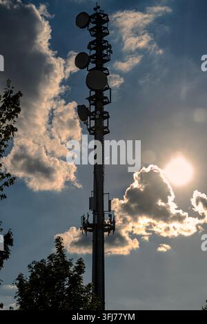 Telekommunikationsmast mit Mobiltelefonantennen vor dramatischem blauem Himmel und Sonnenhintergrund Stockfoto