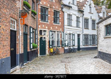 Stadt Brügge in Belgien, Europa. Reizende Kopfsteinpflastergasse mit historischen Backstein- und weißen Fassadengebäuden, mit Fahrrädern und grünen Fensterläden Stockfoto
