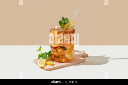 Eistee mit Zitrone, Eis und Minze in einem Glas auf beigem und weißem Hintergrund mit Schatten und Zitronenscheiben. Trendiges Konzept eines erfrischenden Getränks oder Limonade Stockfoto