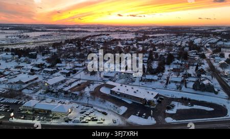 Oranger Sonnenuntergang über der verschneiten Landschaft einer amerikanischen Stadt im Winter. Luftaufnahme mit Geschäften, Nachbarschaft und Ackerland, Penn Township, Pennsylvania. Stockfoto