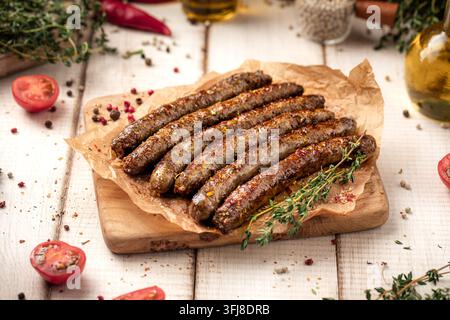 Gegrillte Würste auf Holzbrett mit Kräutern Stockfoto