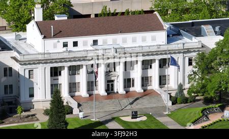 Historisches weißes Gerichtsgebäude mit Säulen, amerikanischer und oregonischer Staatsflagge, die den großen Eingangsstufen flankieren, gepflegter Rasenfläche und grünen Bäumen in der Innenstadt von Rose Stockfoto
