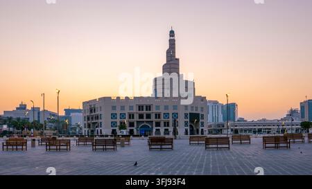 Fanar-Spiritus-Moschee steht prominent hinter einem leeren gepflasterten Platz mit Holzbanken während eines warmen orangefarbenen Sonnenuntergangs in Doha, Katar. Stockfoto