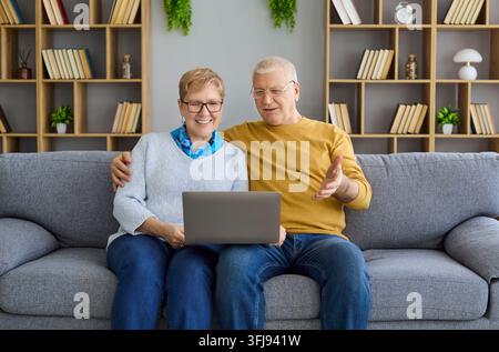 Fröhliches Seniorenehepaar führt Online-Videotelefonie über einen Laptop, während es auf dem Sofa zu Hause sitzt Stockfoto