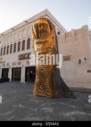 Riesige bronzene Le Pouce-Daumen-Skulptur, die auf einem gepflasterten Platz im Souq Waqif steht Stockfoto