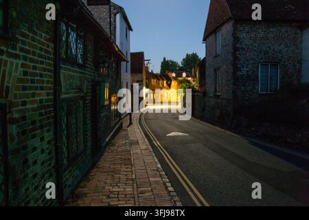Ein ruhiger Abendblick, der die schmale, kurvenreiche historische Straße in Alfriston, East Sussex, hinaufschaut, gesäumt von traditionellen Ziegel- und Flintsgebäuden. Stockfoto