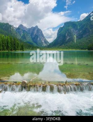 Blick auf den Dobbiaco-See mit kleinem kaskadierendem Wasserfall im Vordergrund, smaragdgrünen Gewässern und Berggipfeln. Bozen, Südtirol, Dolomiten, Italien Stockfoto