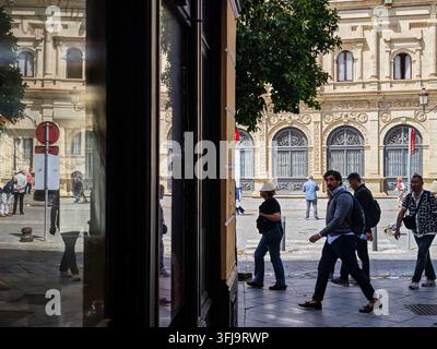 Reflexionen historischer Gebäude und vorbeigehender Fußgänger, sichtbar in einem Schaufenster auf dem San Francisco-Platz in Sevilla, Andalusien, Spanien, die Lebhaftigkeit einfangen Stockfoto