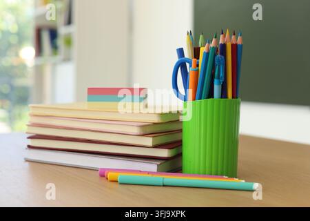 Bücher und Schreibwaren auf einem Holzschreibtisch im Klassenzimmer, Nahaufnahme Stockfoto