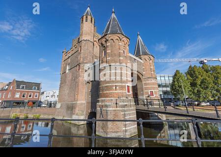Haarlem, Niederlande – 16. August 2026: Niederwinkelaufnahme des mittelalterlichen Amsterdamer Stadttors Amsterdamse Poort mit Backsteintürmen über dem Kanal an einem sonnigen Tag. Stockfoto