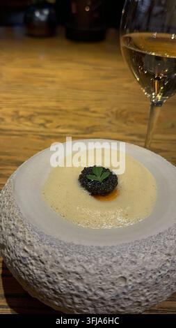 Gourmet-Gericht mit schwarzem Kaviar und einem Glas Weißwein gekrönt. Gourmet-Gericht serviert in einer strukturierten Stein-Schale, mit einer cremigen Sauce, die mit Blätterteig belegt ist Stockfoto