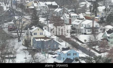 Auto fährt eine schneebedeckte Straße bergauf in einer amerikanischen Vorstadt. Schneesturm im Winter. Luftaufnahme. Schneebedeckte Dächer von Einfamilienhäusern in Massachu Stockfoto