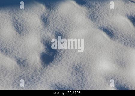 Nahaufnahme-Makroaufnahme von frischem, funkelndem Schnee mit sanft wogenden Schatten und feiner eisiger Textur an einem hellen Wintertag. Stockfoto