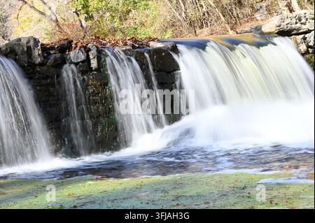 Kleiner Wasserfall stürzt über den Steinwehrüberlauf in einem Herbstwald Stockfoto