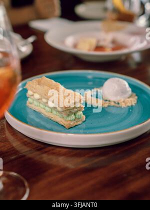 Gourmet-Mille-feuille mit Cremeschichten und Eiscreme, serviert auf einem türkisfarbenen Teller Stockfoto