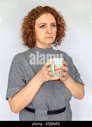 Mittealter Frau hält eine Tasse und sieht nachdenklich aus in einem grauen Pullover-Porträt für Lifestyle-Nutzung Stockfoto