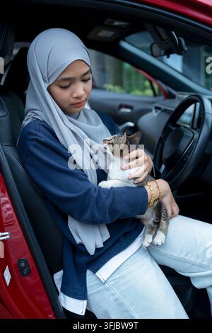 Junge Frau sitzt auf einem Auto mit Katze Stockfoto