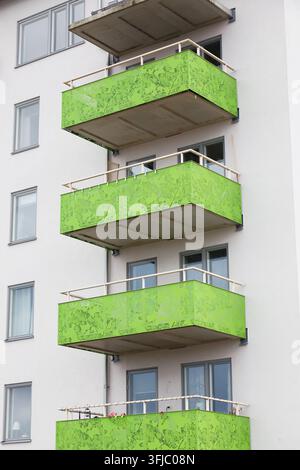 Moderne Wohnhausfassade mit markanten limettengrünen perforierten Metallbalkonen, weißen Außenwänden und mehreren Wohnfenstern. Contem Stockfoto
