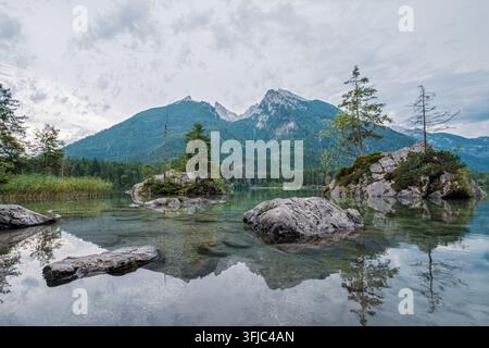 Breite Aufnahme des ruhigen Hintersees in den Bayerischen Alpen, die die klare Wasseroberfläche, kleine Inseln und den Hoher Goll zeigt Stockfoto