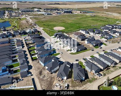 Luftbild des Stadtteils Confederation Park in Saskatoon, das Reihen moderner Häuser mit dunklen Dächern, grünen Rasenflächen und gewundenen Straßen zeigt. Großer offener Bereich Stockfoto