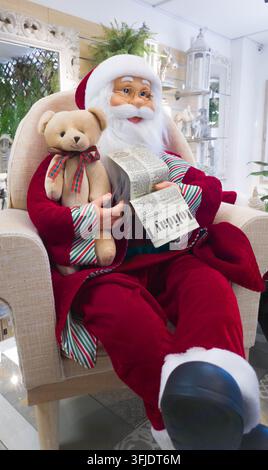 Weihnachtsmannpuppe sitzt in einem Sessel, hält eine Zeitung und einen Teddybär, Dekoration für Weihnachten Stockfoto