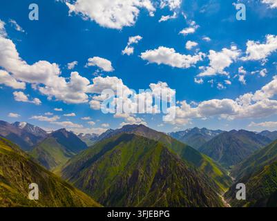 Luftaufnahme zeigt eine weitläufige Bergkette in Kirgisistan. Schroffe Gipfel und grüne Hänge bilden eine atemberaubende Landschaft unter einem strahlend blauen Himmel mit flauschigen Wolken Stockfoto