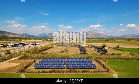 Luftbild einer Solarzellenanordnung, die auf einem ländlichen Feld installiert wurde, mit Bergen und blauem Himmel im Hintergrund, Konzept der erneuerbaren Energie. Stockfoto
