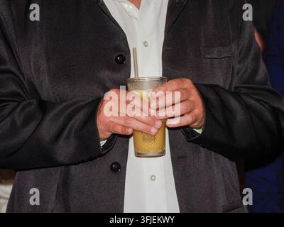 Person, die ein strukturiertes Glas mit einem schaumigen Oranggetränk hält. Stockfoto