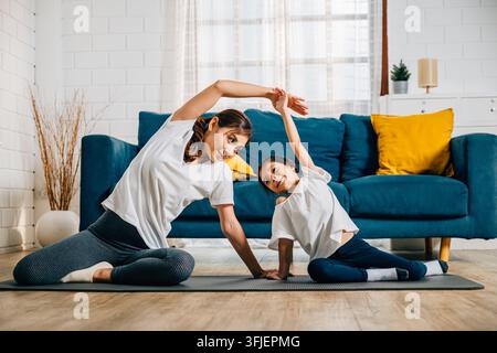 Eine asiatische Mutter lehrt ihre Tochter Yoga in ihrem Wohnzimmer mit Schwerpunkt auf Haltung und Gleichgewicht. Die Familie genießt einen glücklichen und gesunden Lebensstil zusammen Stockfoto