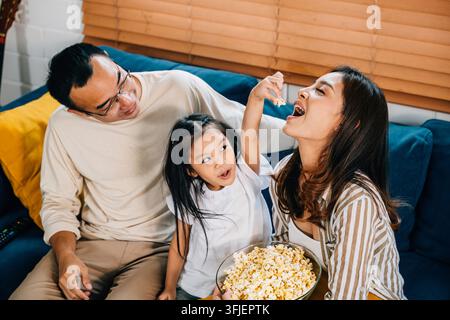 Eine entzückende Familie genießt Fernsehen und Popcorn auf einer gerillten Couch und fördert Momente der Zusammengehörigkeit und Verbundenheit. Vater Mutter Tochter und Geschwister teilen Gelächter Stockfoto