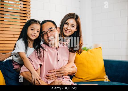 Eine fröhliche Familie in ihrem modernen Zuhause genießt Qualitätszeit auf dem Sofa, das Zusammenhalt zeigt. Eltern Töchter und Geschwister verbinden sich, lachen und umarmen Stockfoto